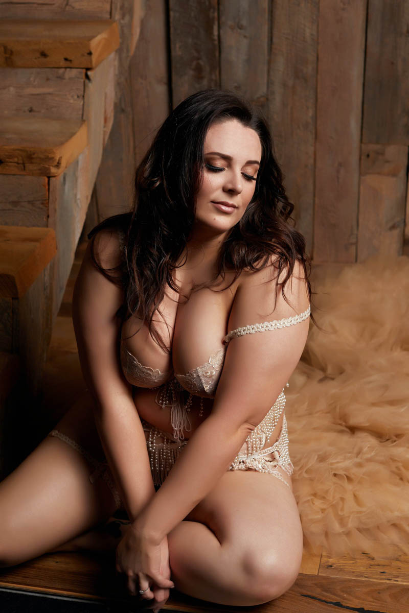 Professional boudoir portrait of plus sized woman sitting in a rustic inspired set
